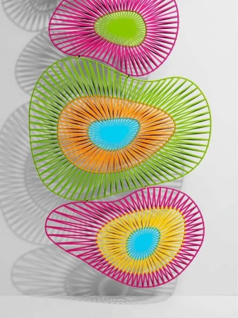 Abstract wall art featuring colorful concentric designs in pink, green, orange, yellow, and blue, casting shadows on a white wall.