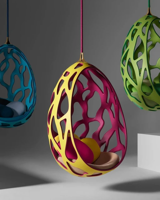 Three colorful hanging cocoon chairs with yellow, pink, blue, and green frames and cushions create a modern and inviting interior space.