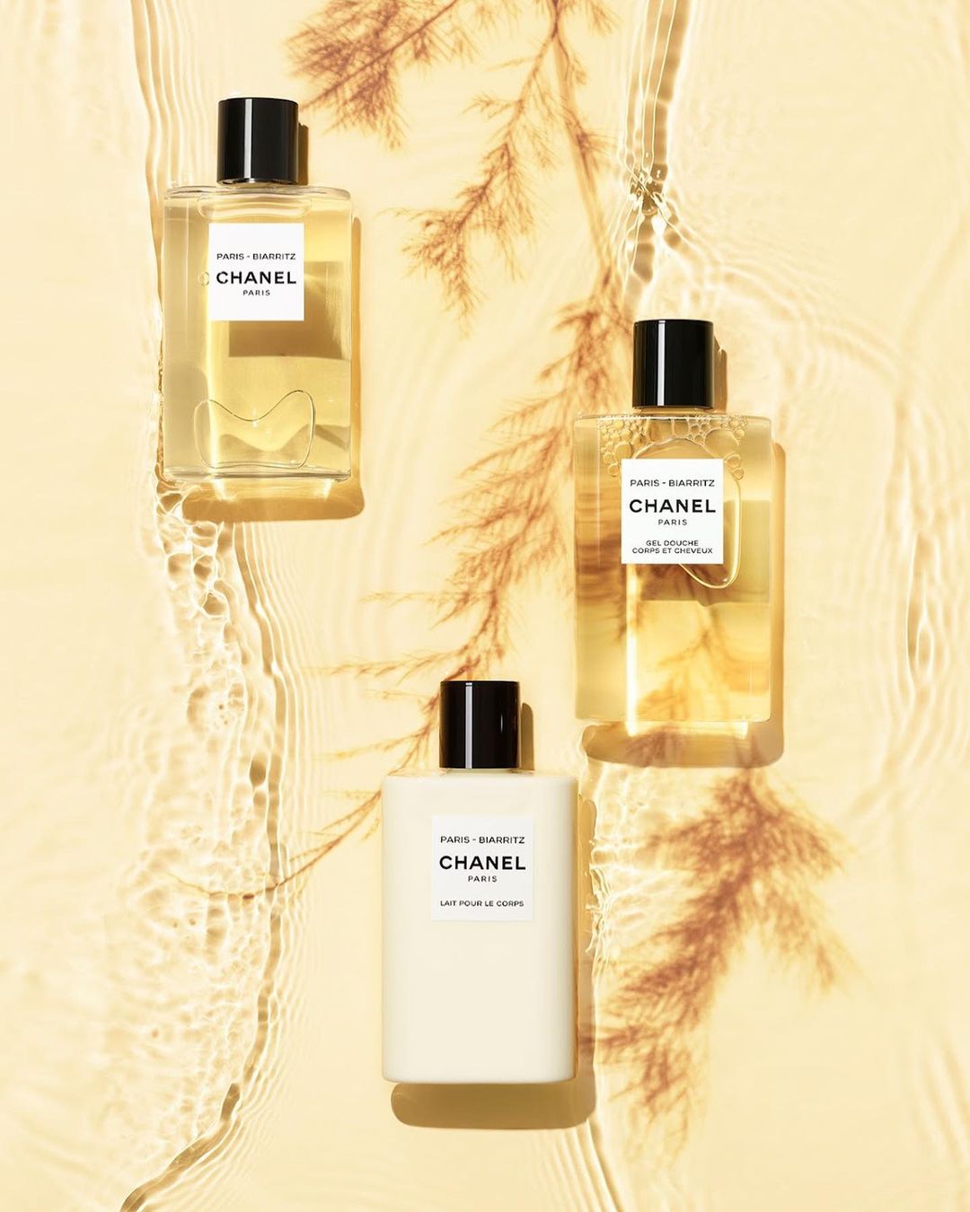 Chanel Paris-Biarritz body care products displayed on a beige surface with light refracting through water adding a shimmering effect.