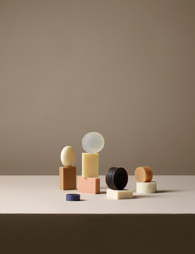 Still life composition with multicolored bars and round shapes of handcrafted soap in a neutral setting against a taupe background.