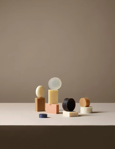 Still life composition with multicolored bars and round shapes of handcrafted soap in a neutral setting against a taupe background.