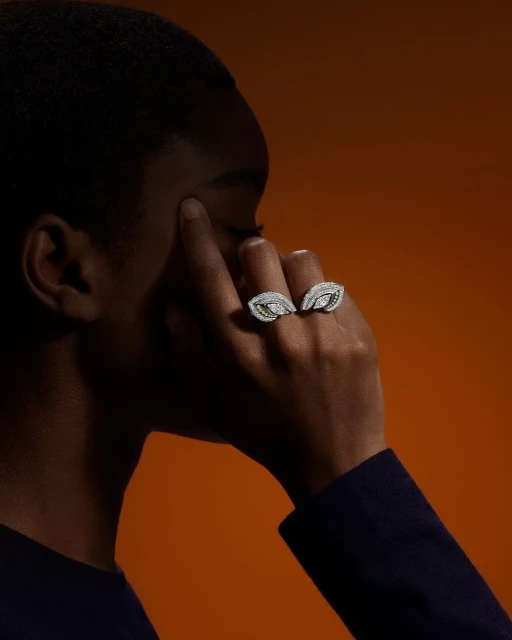 Close-up of a dark-skinned adult female model wearing two leaf-shaped diamond rings against a deep orange background.