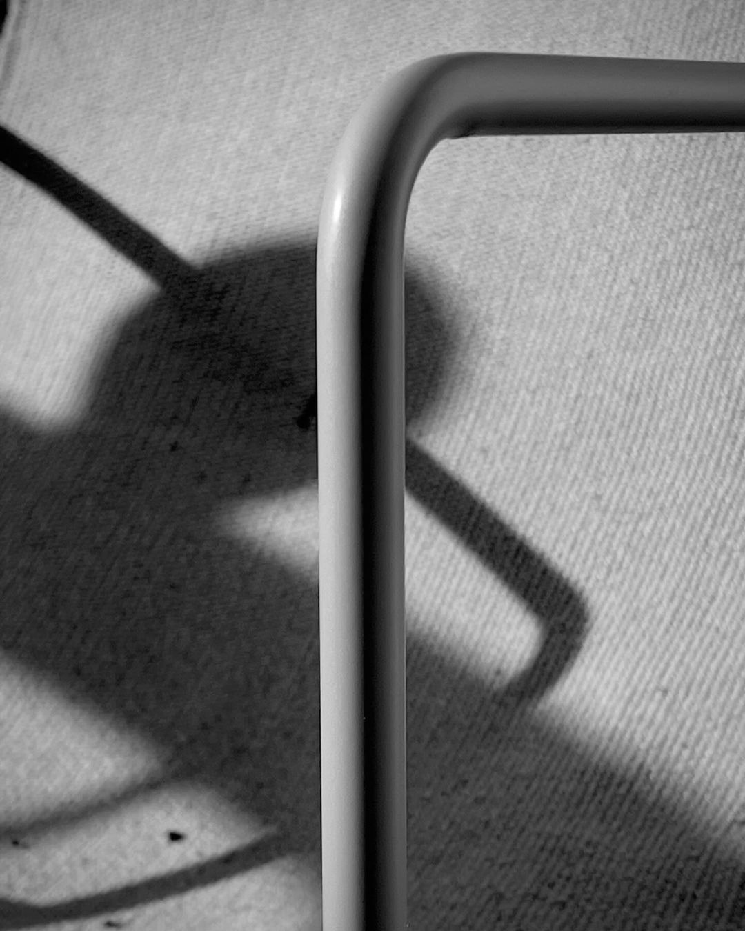 Monochromatic shot of a white metal frame creating a right angle with a shadow visible on the textured gray background behind it.