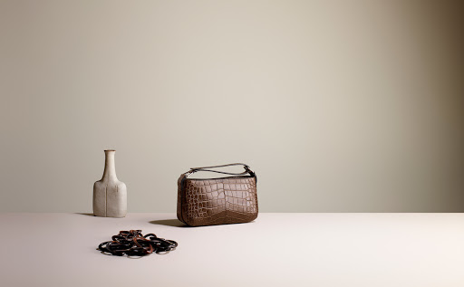 Brown crocodile-patterned handbag sits on a white surface, next to a beige vase and a collection of black elastic hair ties.