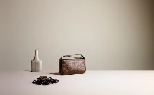 Brown crocodile-patterned handbag sits on a white surface, next to a beige vase and a collection of black elastic hair ties.