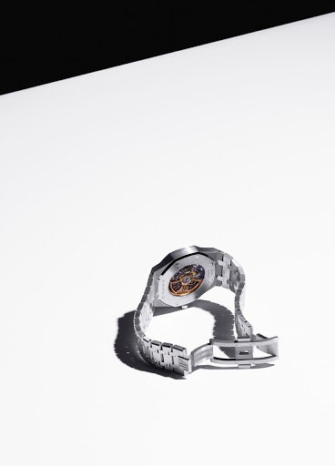 Elevated view of a stainless-steel wristwatch on a white surface, with black background shadow at top. Watch face is visible.