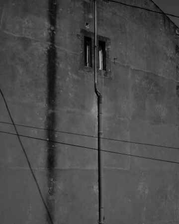 Monochrome shot of an exterior building wall with a window, drainpipe, and power lines, showcasing architectural detail and urban texture.