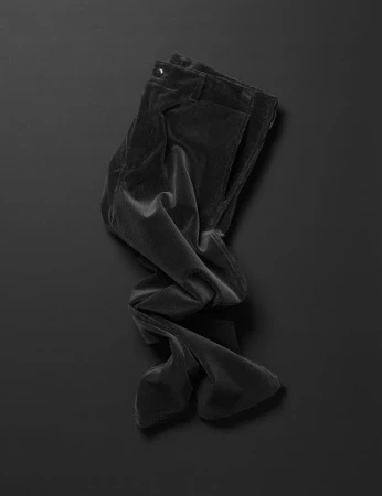 Elevated studio shot of folded, dark corduroy pants on a black background with soft shadows. Minimalist fashion photography.