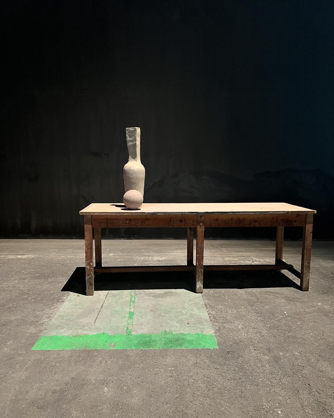Still life of a ceramic bottle and sphere on a wooden table against a dark background, creating a minimalist and artistic composition.