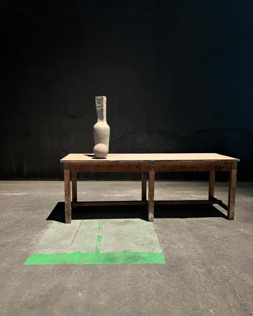 Still life of a ceramic bottle and sphere on a wooden table against a dark background, creating a minimalist and artistic composition.