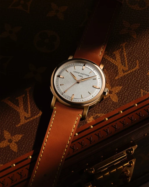 Gold Louis Vuitton watch with a brown leather strap on a Louis Vuitton trunk with the LV monogram pattern. Timepiece photography.