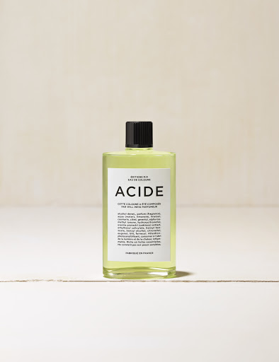 Close-up studio shot of a bottle of ACIDE eau de cologne on a white surface with a neutral-toned background.