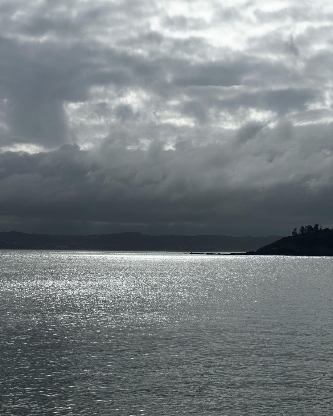 Overcast sky over a calm body of water with a hint of land in the distance, creating a tranquil, moody seascape.
