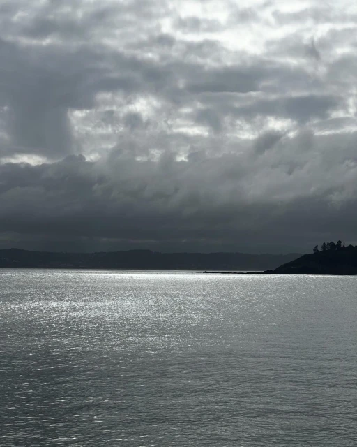 Overcast sky over a calm body of water with a hint of land in the distance, creating a tranquil, moody seascape.