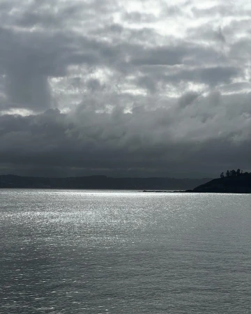 Overcast sky over a calm body of water with a hint of land in the distance, creating a tranquil, moody seascape.