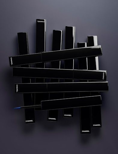 An arrangement of glossy black Chanel eyeliner packaging tubes with visible white logo text against a dark grey background.