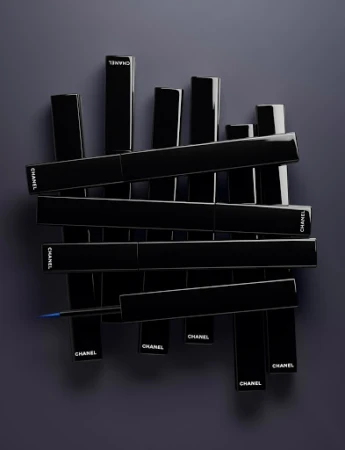 An arrangement of glossy black Chanel eyeliner packaging tubes with visible white logo text against a dark grey background.