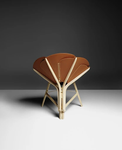 Tan folding chair with beige wood frame against a dark gray and white gradient background. Modern furniture design with unique style.