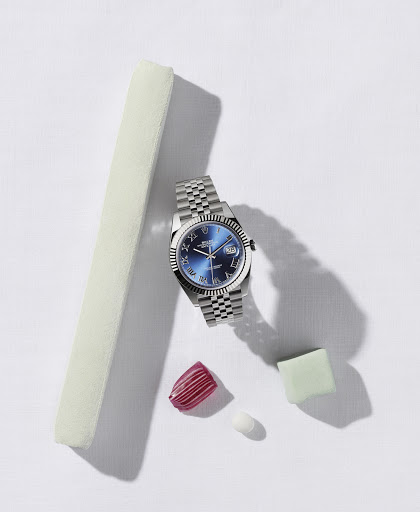 Wristwatch with a blue face and silver band displayed with decorative items including a pink nail and pale green cube on white.