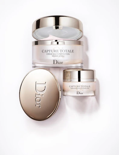 Overhead studio shot of four Dior Capture Totale skincare products, including face creme, serum, and compact, on a bright white background.