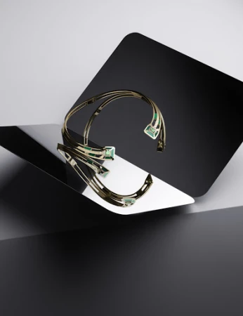Elegant gold choker necklace with green gemstones displayed on a reflective surface with a geometric black and gray background in studio lighting.