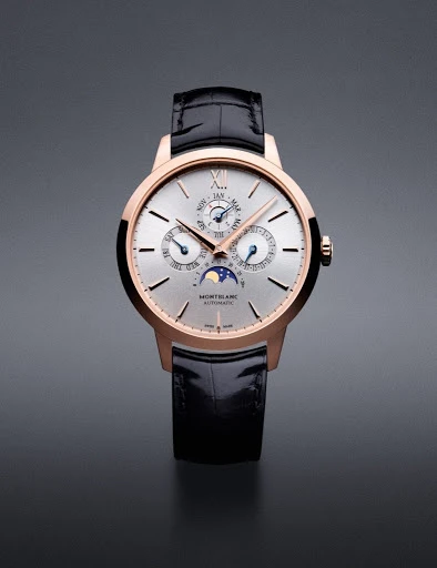 Elegant gold-tone Montblanc wristwatch with black leather band displayed on a gray background. The watch face features subdials and moon phase.