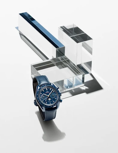 Blue luxury wristwatch on a matching leather strap, positioned against clear acrylic blocks in a studio setting with bright lighting.