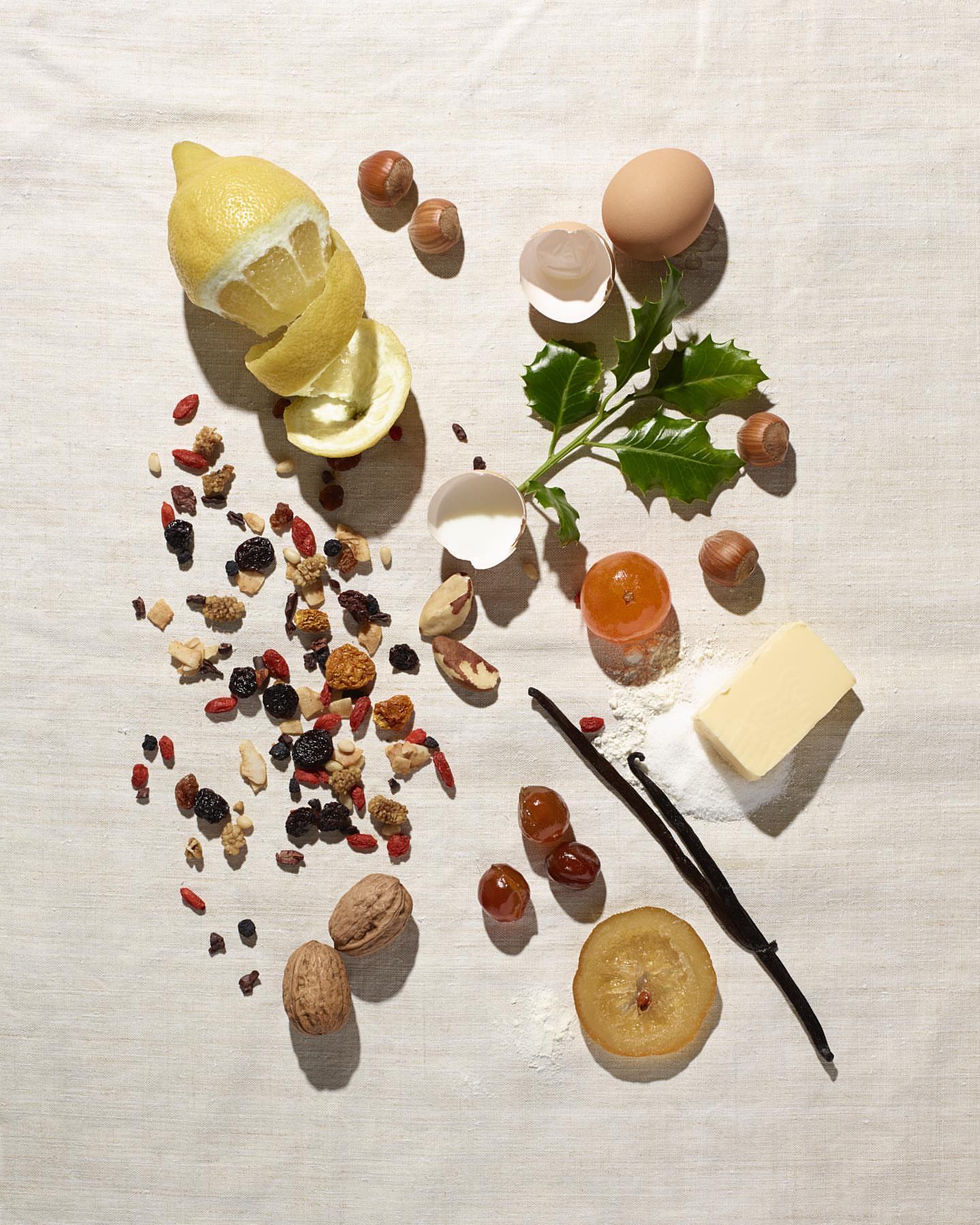 Overhead still life of lemons, nuts, and baking ingredients like eggs, vanilla, and butter on a white tablecloth. Food photography.