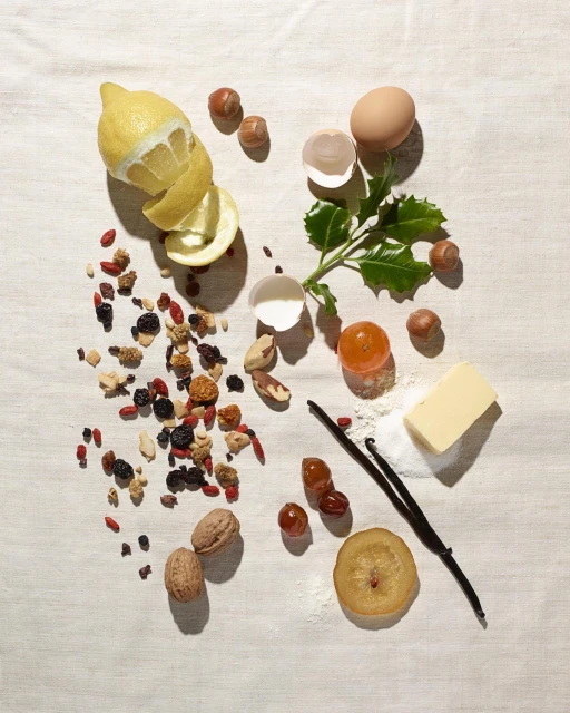 Overhead still life of lemons, nuts, and baking ingredients like eggs, vanilla, and butter on a white tablecloth. Food photography.