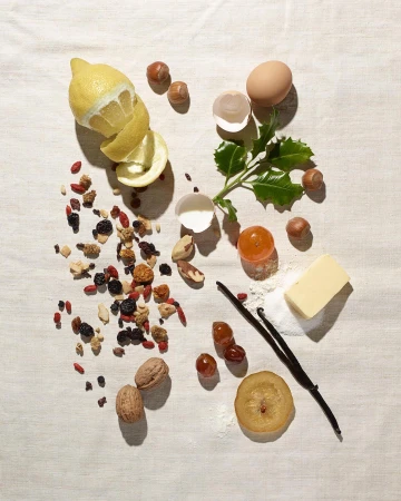 Overhead still life of lemons, nuts, and baking ingredients like eggs, vanilla, and butter on a white tablecloth. Food photography.