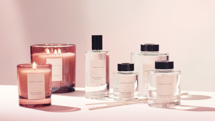 Candles and home fragrances from Zara Home, featuring pure gardenia scent in glass containers with wooden diffuser sticks, on a pink surface.