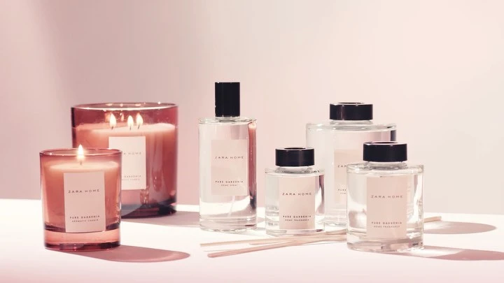 Candles and home fragrances from Zara Home, featuring pure gardenia scent in glass containers with wooden diffuser sticks, on a pink surface.