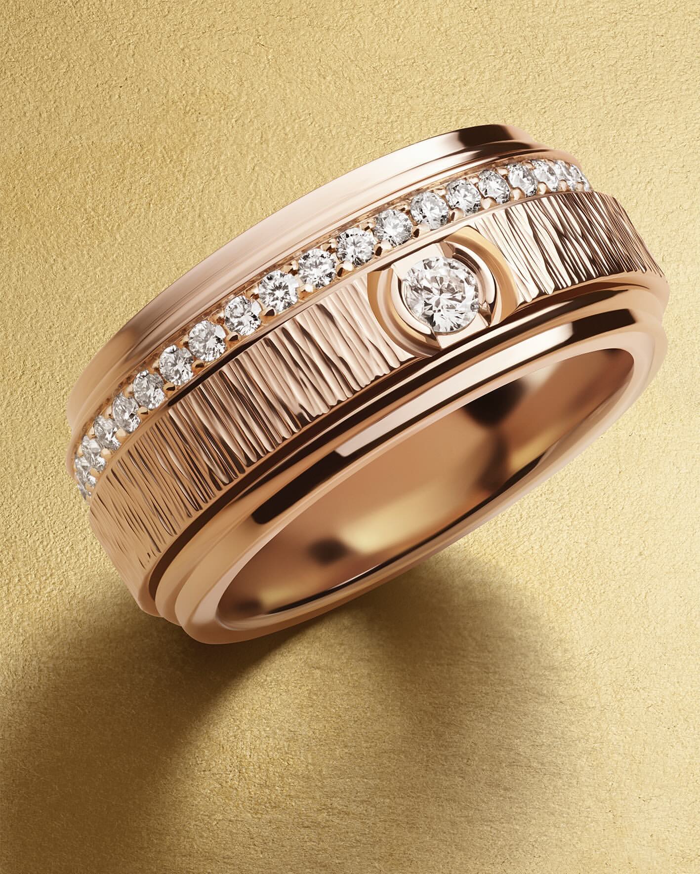 Close-up of a rose gold ring featuring a textured band, diamond accents, and a central round diamond on a neutral gold surface.