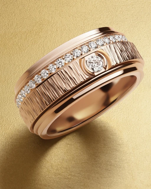 Close-up of a rose gold ring featuring a textured band, diamond accents, and a central round diamond on a neutral gold surface.