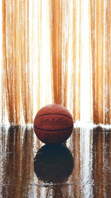 Close-up of a Louis Vuitton NBA basketball on a wet surface with an orange string curtain backdrop, creating an artful composition.
