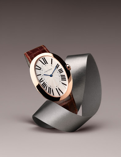 Elegant rose gold Cartier watch with a white face and brown leather strap, showcased against a silver ribbon and a soft grey background.
