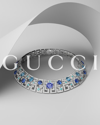 Elegant white gold and blue sapphire necklace featuring the Gucci logo, set against a light grey background with a floating white paper accent.