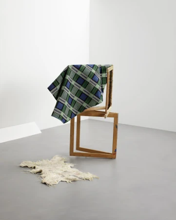 Still life of a geometric composition featuring a blue and green plaid textile draped over wooden frames, with a sheepskin on the floor.