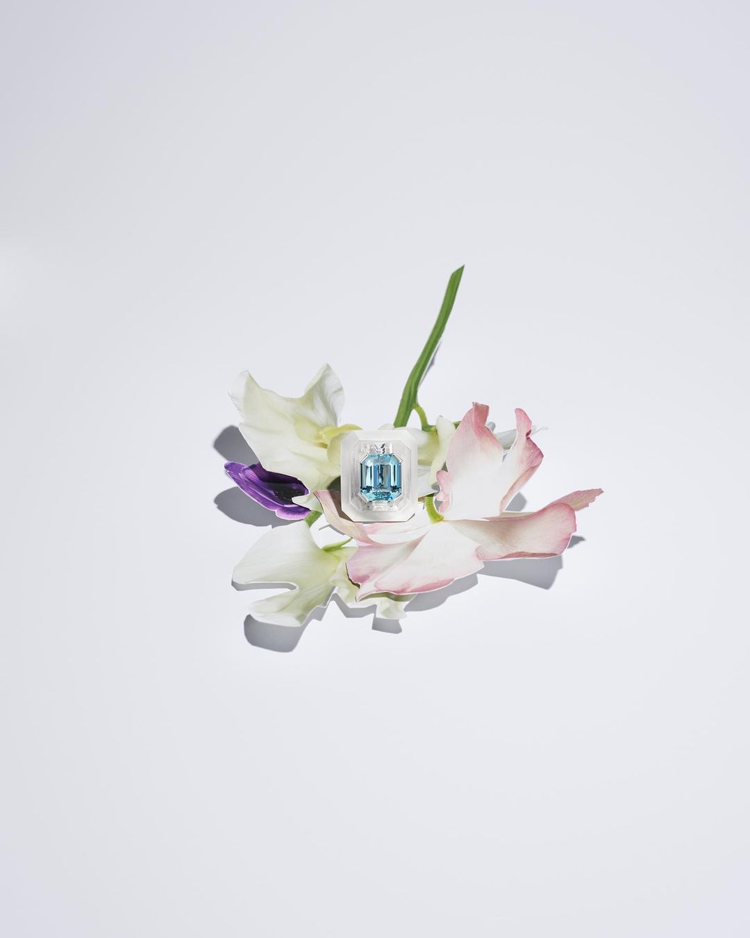Close-up of an aquamarine gemstone pendant on a stem with petals in soft light, showcasing its jewelry design on a white background.