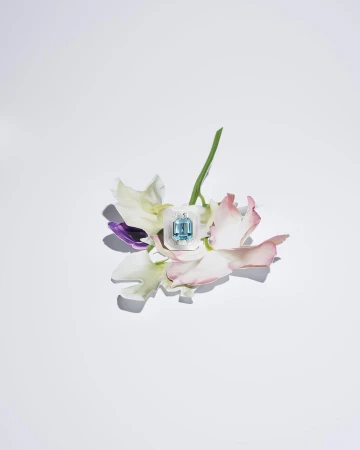 Close-up of an aquamarine gemstone pendant on a stem with petals in soft light, showcasing its jewelry design on a white background.