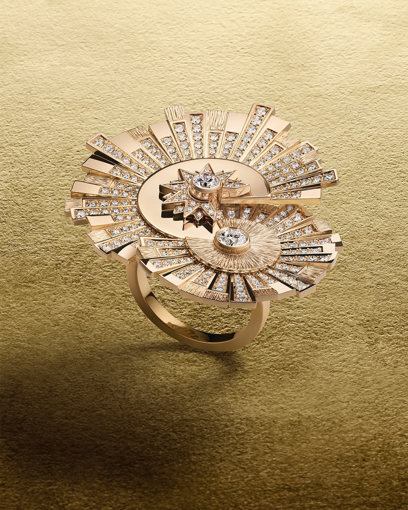 Close-up studio shot of a gold ring featuring a geometric sunburst design with sparkling diamond accents against a gold background.