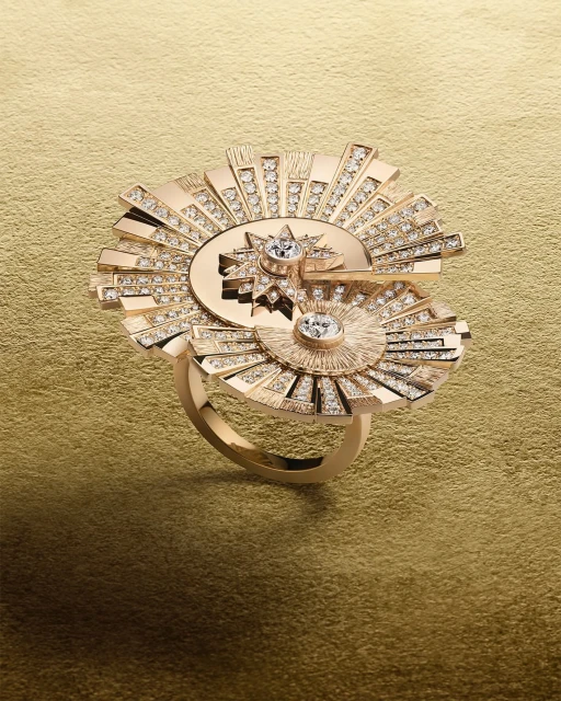Close-up studio shot of a gold ring featuring a geometric sunburst design with sparkling diamond accents against a gold background.