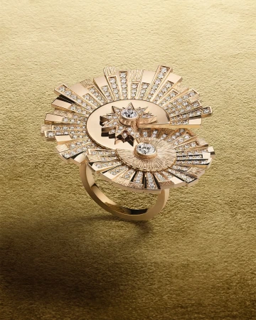Close-up studio shot of a gold ring featuring a geometric sunburst design with sparkling diamond accents against a gold background.