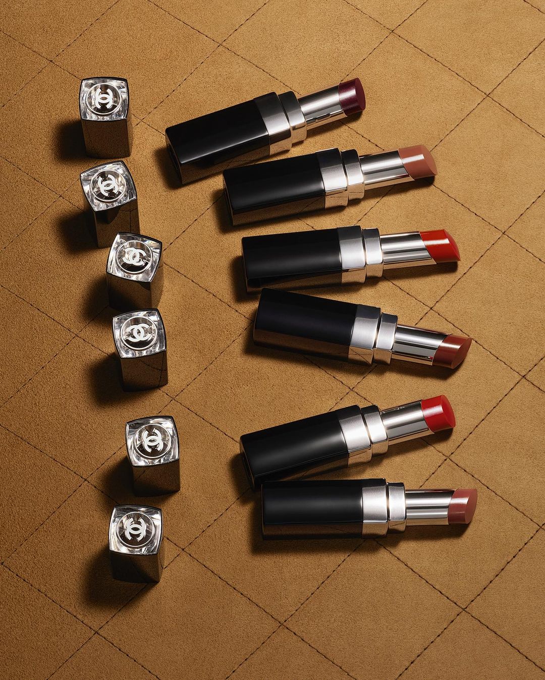 Arrangement of Chanel lipsticks in varying shades on a tan quilted surface, showcasing beauty and cosmetic product photography.