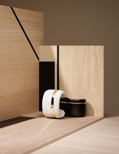 Minimalist beauty still life with a white bangle bracelet and a black cosmetic jar against geometric wood panels.