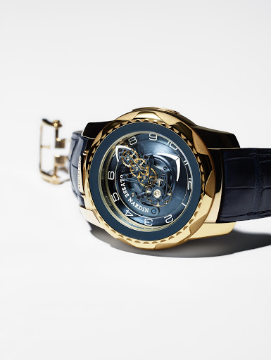 Elegant gold Ulysse Nardin watch with intricate mechanical movement and black leather strap displayed on a white surface.