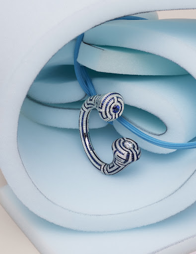 Close-up of a decorative silver and blue pendant necklace with a maze-like design, set against a light blue foam background.