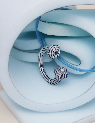 Close-up of a decorative silver and blue pendant necklace with a maze-like design, set against a light blue foam background.