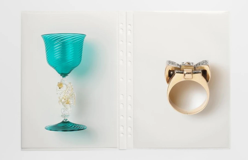 Turquoise glass with a seahorse stem sits next to a gold ring with diamonds, presented in a clear, organized display.