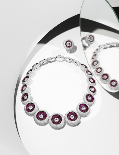 Elegant jewelry shot: A silver necklace and ring with ruby and diamond accents are displayed on a white surface with mirror reflections.